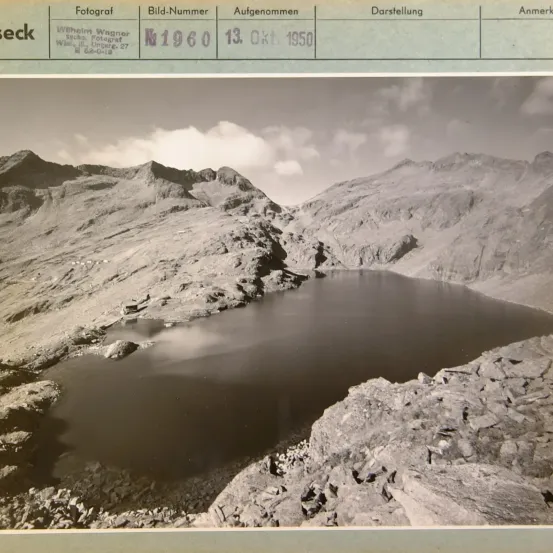 Ein Schwarz-Weiß-Foto zeigt einen See zwischen felsigen Bergen. Über dem Bild befindet sich eine Tabelle mit Details: Fotograf Wilhelm Wagner, Bildnummer K1960, aufgenommen am 13. Oktober 1950.