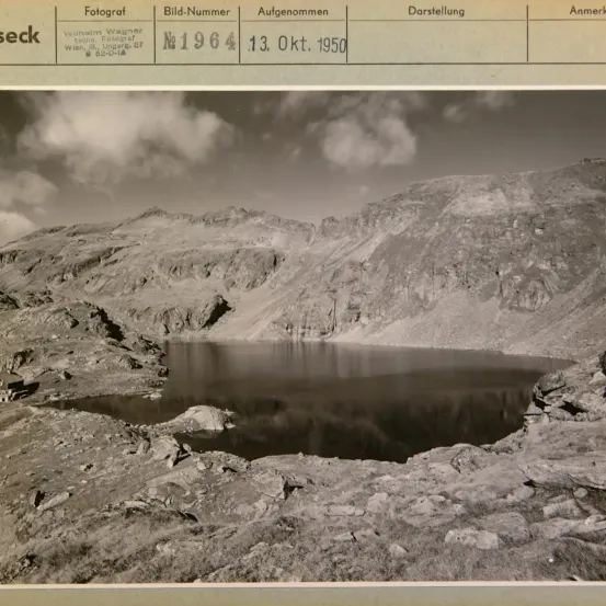 Ein Schwarz-Weiß-Foto zeigt eine Berglandschaft mit einem See in der Mitte. Ein Wasserzeichen zeigt, dass es am 13. Oktober 1950 aufgenommen wurde.