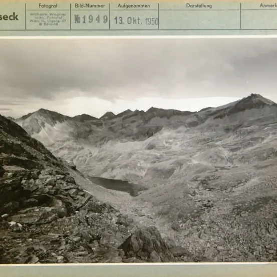 Ein Foto von Bergen mit felsigem Gelände und einem See, aufgenommen am 13. Oktober 1950 von Wilhelm Wagner. Das Bild trägt die Bild-Nummer N1949.