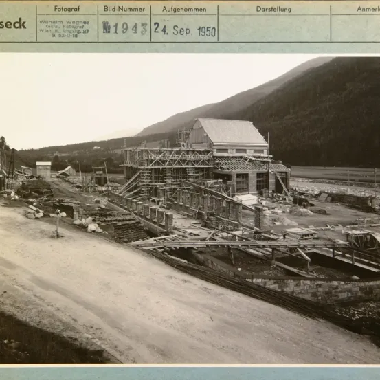Ein Bild einer Baustelle mit einem Gebäude im Bau. Im Hintergrund sind Berge zu sehen. Datum: 24. September 1950.