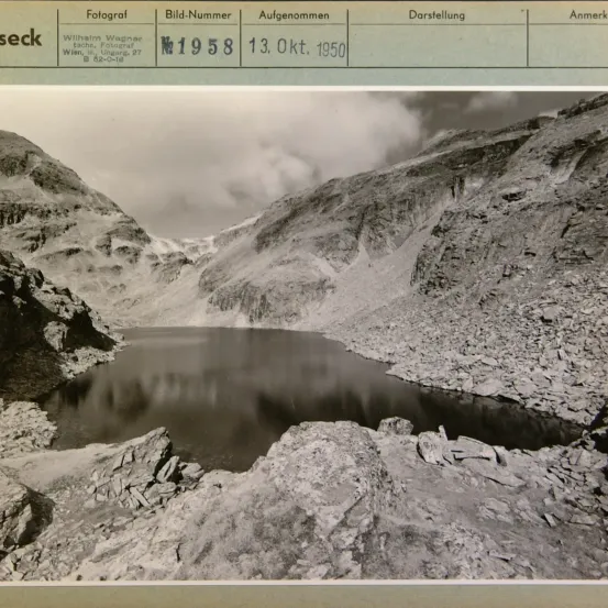 Schwarz-Weiß-Foto eines Bergsees. Das Bild ist mit 'Aufgenommen 13. Okt. 1950' und 'Fotograf Wilhelm Wagner' beschriftet. Das Foto wurde bei 82-0-18 aufgenommen.