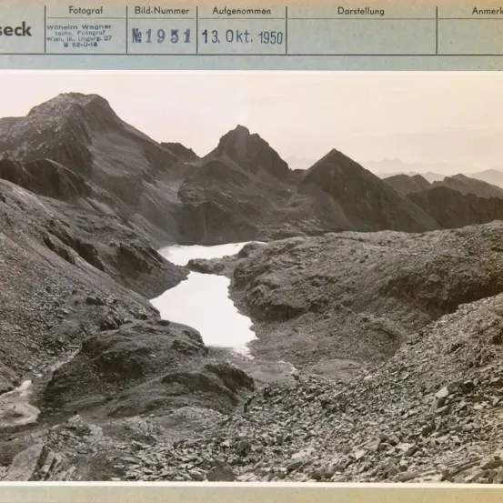 Schwarz-Weiß-Foto einer bergigen Landschaft mit einem Fluss, der zwischen den Bergen fließt. Das Bild ist mit dem Namen des Fotografen, Wilhelm Wagner, und dem Datum der Aufnahme, 13. Oktober 1950, beschriftet.