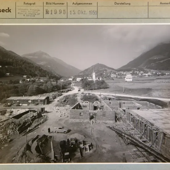 Schwarz-Weiß-Foto einer Baustelle mit Bergen im Hintergrund. Das Foto ist vom 15. Oktober 1950 und enthält Details wie den Namen des Fotografen und die Bildnummer.