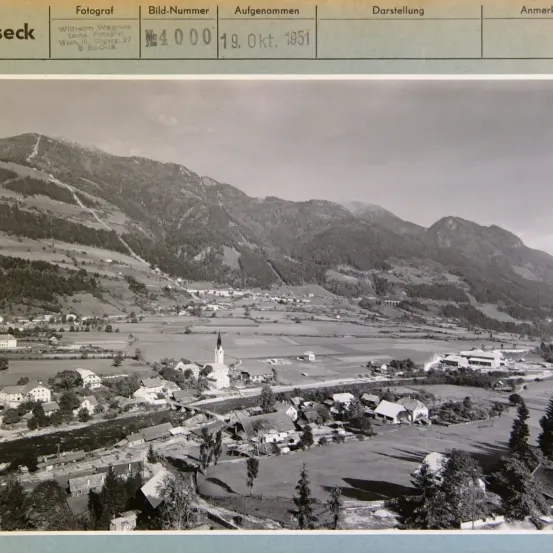 Ein Foto einer Stadt mit der Bildnummer 4000, aufgenommen am 19. Oktober 1951. Es zeigt ein Tal mit Bergen und einem Dorf mit einer Kirche.