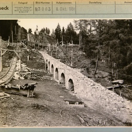 Schwarz-Weiß-Foto einer Baustelle mit Steinbrücke und Gleisen, beschriftet mit Fotografenname und Datum.