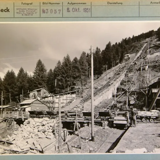 Schwarz-Weiß-Foto von 1951, das eine Baustelle mit steilem Hang, mehreren Gebäuden und verschiedenen Materialien zeigt.