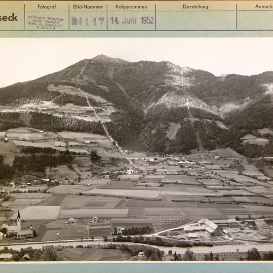 Ein Schwarz-Weiß-Luftbild mit der Aufschrift 'Fotograf' zeigt eine Berglandschaft mit einem Dorf darunter, datiert auf den 14. Juni 1952.