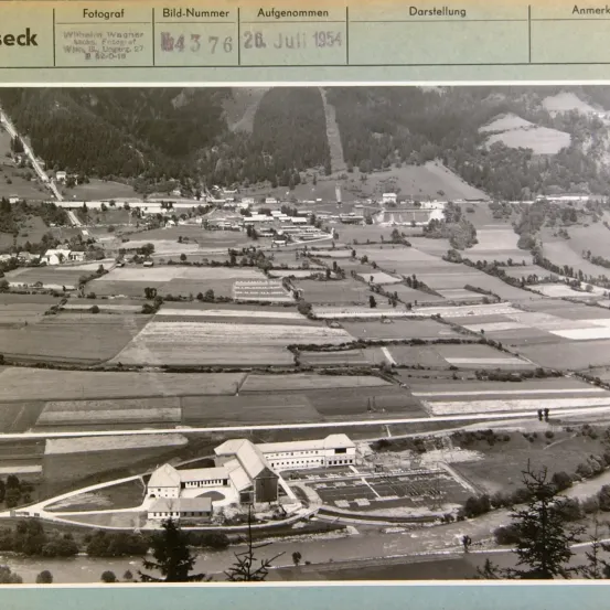 Luftaufnahme eines Dorfes und Ackerlandes, aufgenommen am 28. Juli 1954. Es zeigt ein kleines Dorf mit mehreren Gebäuden und einem großen landwirtschaftlichen Gebiet.