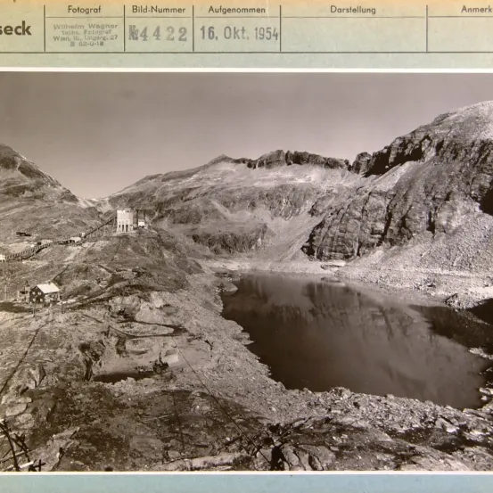 Schwarz-Weiß-Foto einer Berglandschaft mit einem See und einem Haus. Das Foto wurde am 16. Oktober 1954 aufgenommen.