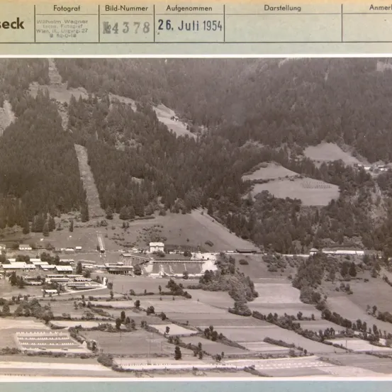 Das Bild ist eine Fotografie mit der Bezeichnung 'Fotograf' und der Identifikationsnummer 'M4378'. Es wurde am 26. Juli 1954 aufgenommen. Das Bild zeigt eine Landschaftsansicht mit einem Gebirgszug, durch den eine Straße schlängelt, umgeben von Bäumen und Vegetation.