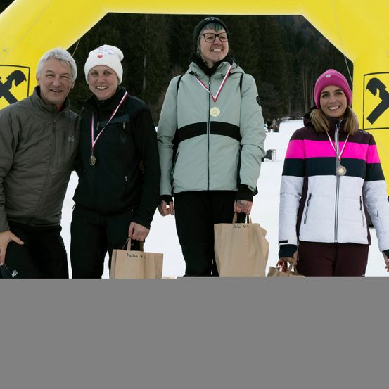 Vier Personen stehen vor einem gelben X-Banner, alle tragen Medaillen. Sie lächeln und sind in Winterkleidung gekleidet.