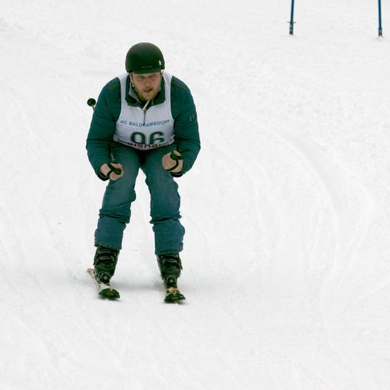 Ein Skifahrer mit grünem Helm fährt den Schneehang hinunter, Nummer 96 auf seiner Jacke.