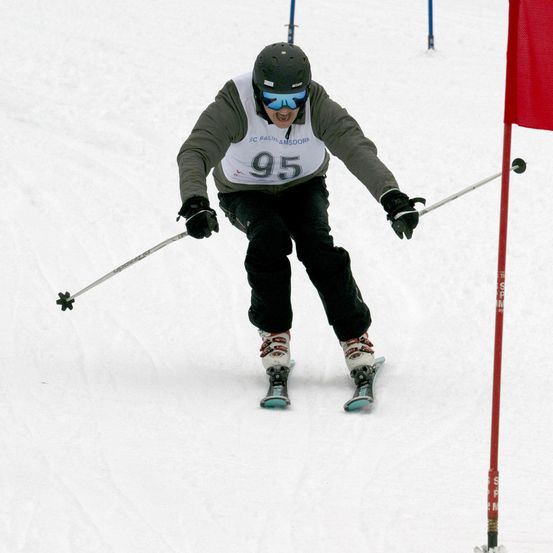 Ein Skifahrer, der ein graues und weißes Trikot mit der Nummer 95 trägt, fährt einen schneebedeckten Hang hinunter und hält Skistöcke.