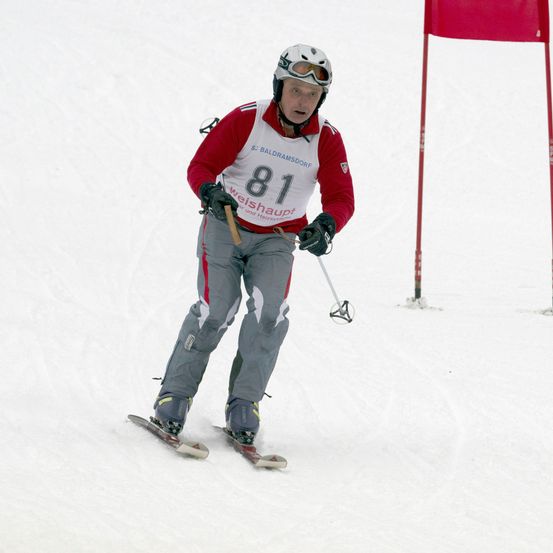 Ein Skifahrer in einem roten und weißen Trikot mit der Nummer 81 auf dem Rücken fährt einen schneebedeckten Hang hinunter.