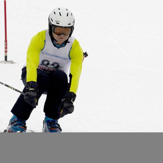Ein Skifahrer mit einem weißen Helm mit der Nummer 92 und einem Skistock in der Schneelandschaft.