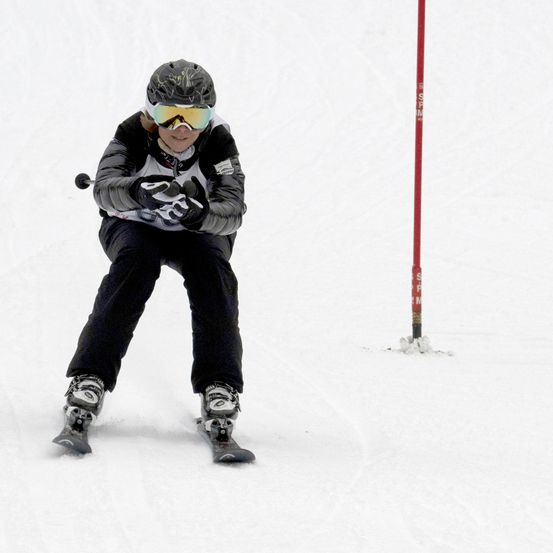 Ein Skifahrer in einer schwarzen und weißen Kleidung fährt einen schneebedeckten Hang hinunter. Er trägt eine Schutzbrille, einen Helm und Handschuhe.