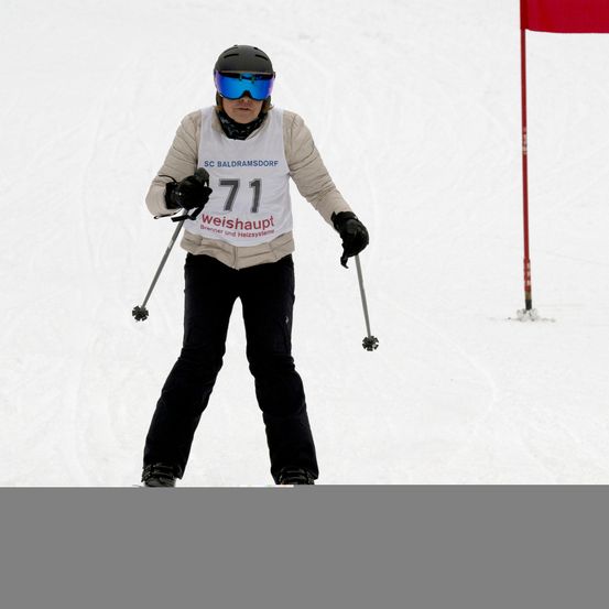 Ein Skifahrer mit einem weißen Shirt, auf dem '71' und 'weishaupt' steht, fährt mit Skistöcken einen verschneiten Hang hinunter.