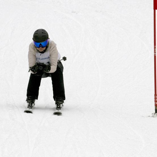 Ein Skifahrer in schwarzer und weißer Kleidung mit blauen Goggles und einem schwarzen Helm fährt den Schneehang hinunter. Er ist leicht nach vorne gebeugt.