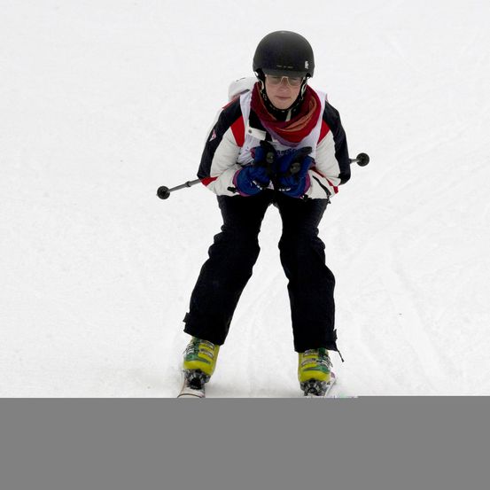 Ein Skifahrer in einer weißen und roten Jacke und schwarzen Hosen fährt einen verschneiten Hang hinunter, trägt einen schwarzen Helm und blaue Handschuhe.