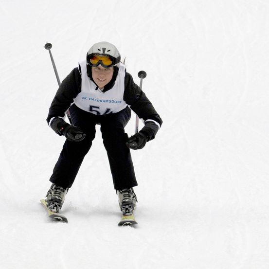Ein Skifahrer mit SC Baldramsdor Skianzug und Skibrille fährt den schneebedeckten Hang hinunter.