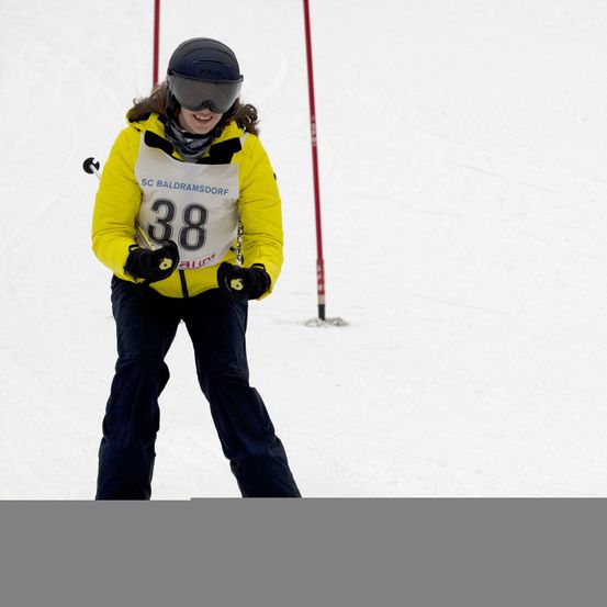Ein Skifahrer in einem gelben Jacket mit der Nummer 38 und einem schwarzen Helm fährt den Schneehang hinunter.