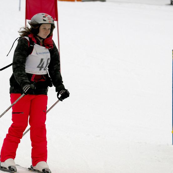 Eine Skifahrerin mit der Nummer 48 trägt einen Helm und rote Skihosen beim Skifahren auf einem verschneiten Hang. Ein roter Flagge befindet sich hinter ihr.