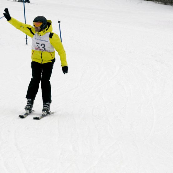 Ein Skifahrer in einem gelben Jacke mit der Nummer 53 posiert für ein Foto auf einer verschneiten Piste.