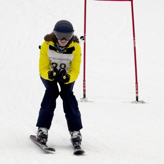 Ein Skifahrer in einem gelben Jacke und Skibrille navigiert eine Slalom-Strecke und fährt zwischen zwei roten Pfosten hindurch.