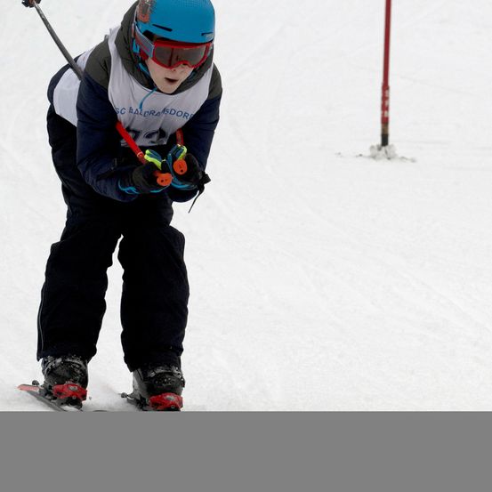 Ein junger Skifahrer fährt im Wettbewerb bergab. Mit blauem Helm und Schutzbrille hält der Skifahrer Skistöcke.