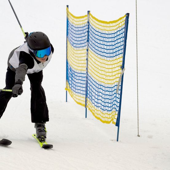 Ein Skifahrer mit schwarzem Helm und Schutzbrille navigiert durch ein gelbes und blaues Hindernis auf einer verschneiten Piste.