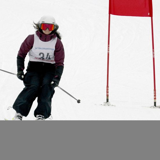 Ein Skifahrer mit weißem Helm und Schutzbrille fährt einen Schneehang hinunter und passiert eine rote Fahne.