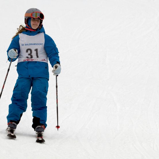 Ein Skifahrer in einem blauen Outfit mit der Nummer 31, Schutzbrille und Handschuhen, der einen verschneiten Hang hinunterfährt.
