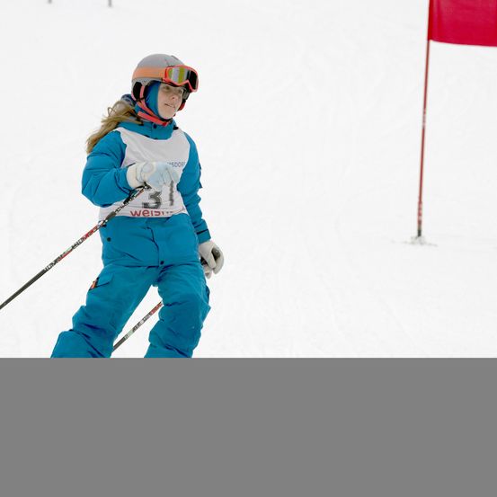 Eine Skifahrerin in blauer Skiausrüstung fährt auf einer verschneiten Piste. Sie hält Skistöcke und trägt eine Skibrille und einen Helm. Die Nummer 31 ist auf ihrer Kleidung sichtbar.