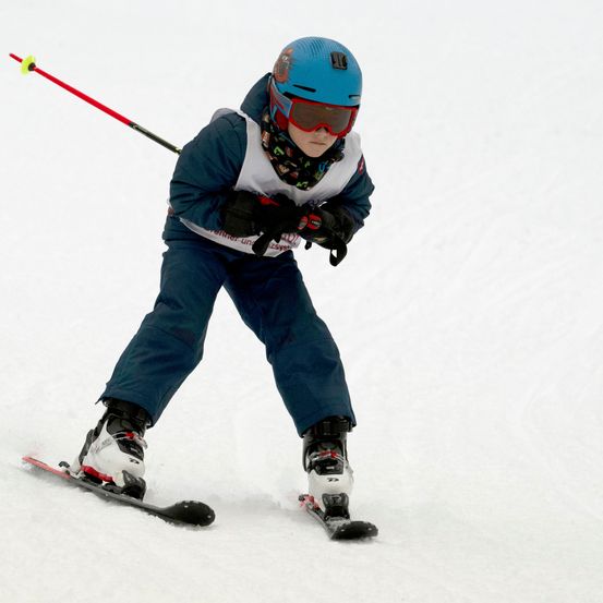 Ein junger Skifahrer mit blauem Helm und Sonnenbrille fährt einen verschneiten Hang hinunter.