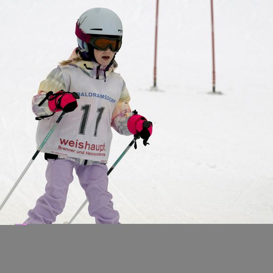Ein junger Skifahrer in einem weißen Helm und Schutzbrille fährt bergab, Nummer 11 auf dem Trikot.