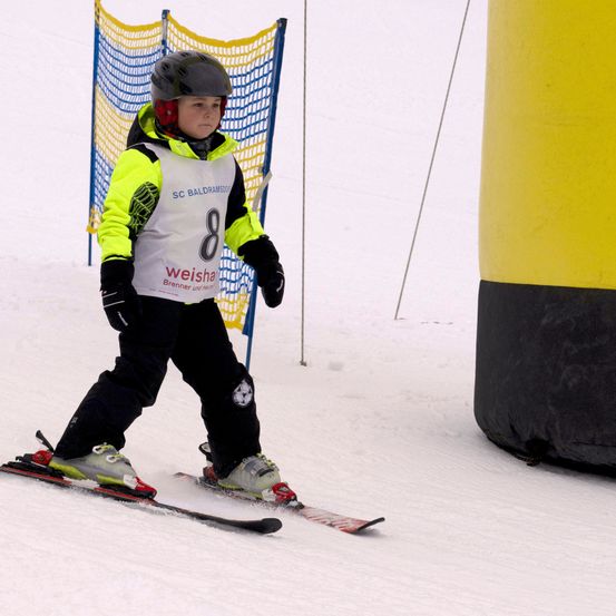 Ein Kind skilt einen schneebedeckten Hang hinunter und trägt eine gelb-schwarze Jacke mit der Nummer 8.