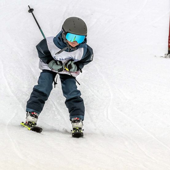 Ein junger Skifahrer, mit Helm, Brille und Skiausrüstung, fährt den Schneehang hinunter.