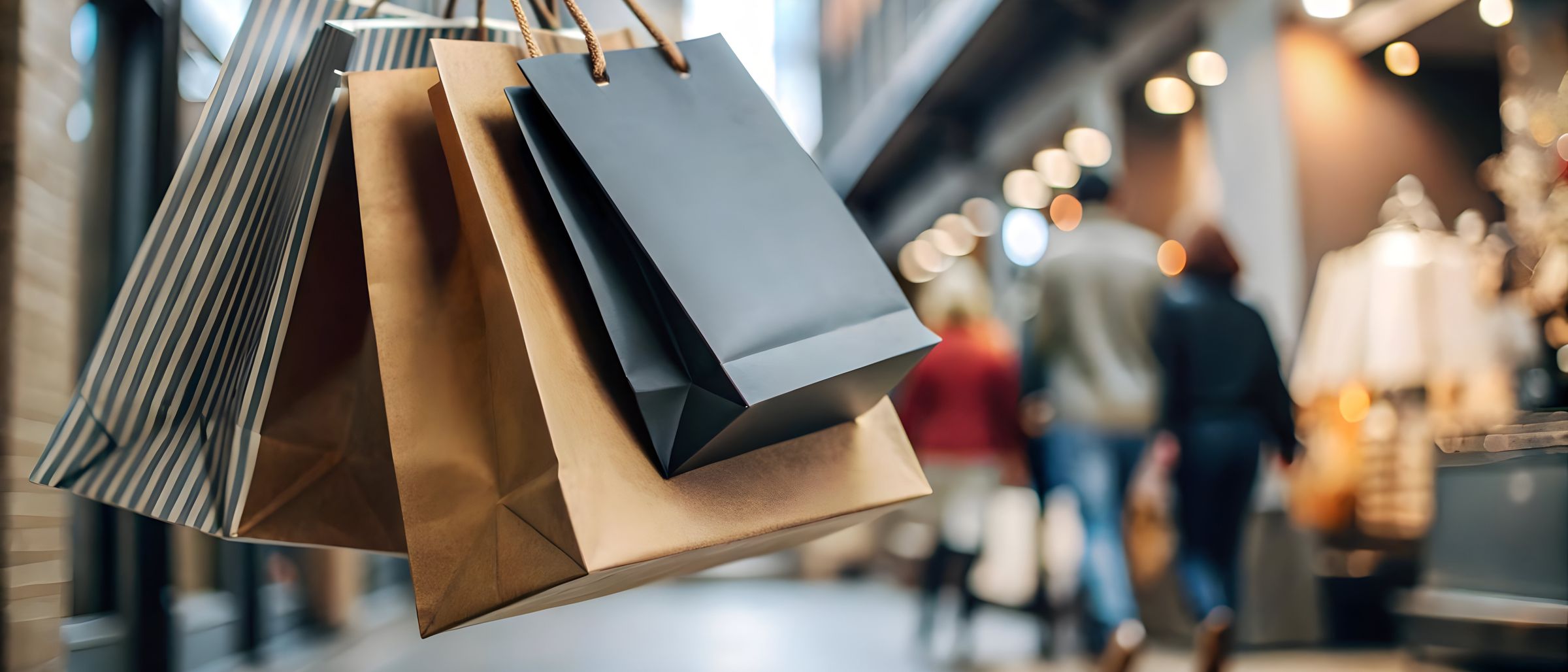 Mehrere Einkaufstüten hängen an Griffen. Im Hintergrund gehen Menschen, leicht unscharf.