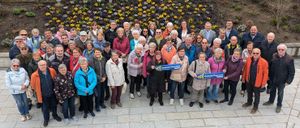 Eine Gruppe älterer Personen, alle in Winterkleidung, posiert für ein Foto vor einer mit Blumen geschmückten Wand. Einige von ihnen halten Schilder mit der Aufschrift 'NEIN'.