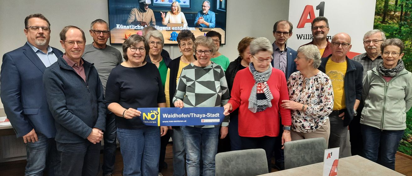 Eine Gruppe von Menschen versammelt sich, hält ein blaues Banner mit NO 5 und Waidhofen/Thaya-Stadt. Sie lächeln und posieren für ein Foto im Besprechungsraum.