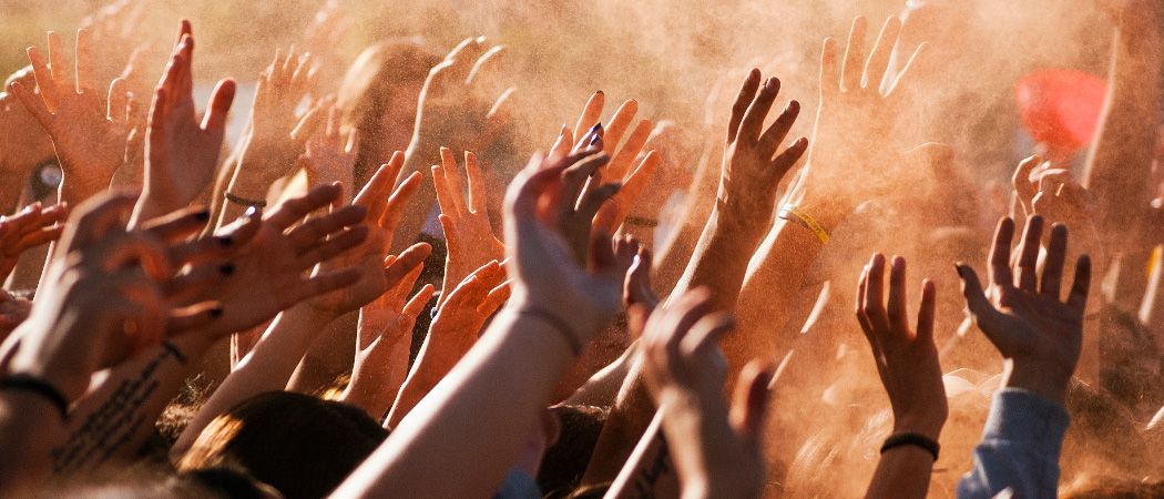 Eine große Menschenmenge bei einem Konzert, die Hände hebend und die Musik genießend. Staub und Rauch füllen die Luft.