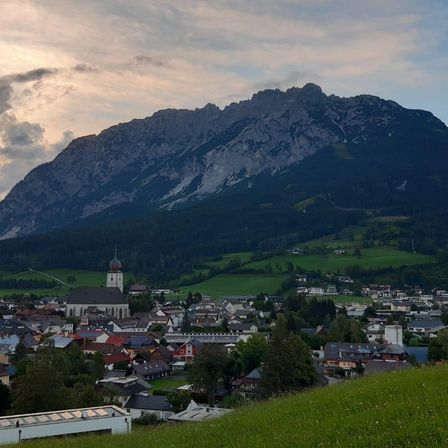 Eine kleine Stadt mit einer Kirche und einem großen Berg im Hintergrund. Die Stadt ist von grünen Feldern und Bäumen umgeben.