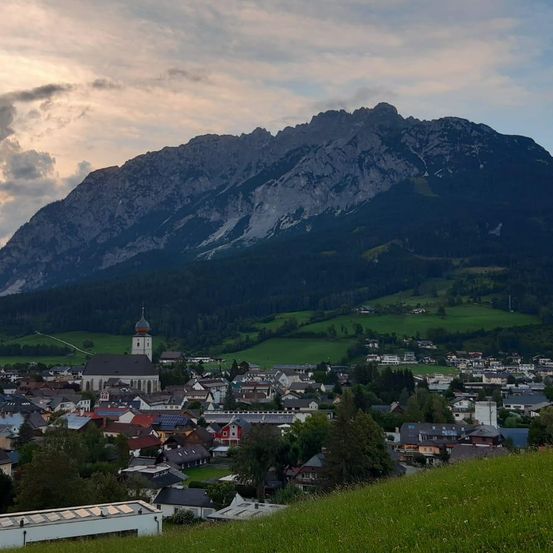 Eine kleine Stadt mit einer Kirche und einem großen Berg im Hintergrund. Die Stadt ist von grünen Feldern und Bäumen umgeben.