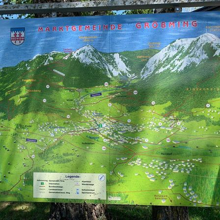 Eine Karte der Gemeinde Großgmain wird auf einem Baumstumpf ausgestellt. Die Karte zeigt Berge, Städte und Wege. Eine Legende auf der Karte enthält Informationen über verschiedene Arten von Straßen und Sehenswürdigkeiten.