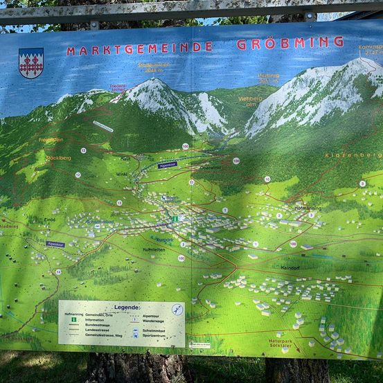 Eine Karte der Gemeinde Großgmain wird auf einem Baumstumpf ausgestellt. Die Karte zeigt Berge, Städte und Wege. Eine Legende auf der Karte enthält Informationen über verschiedene Arten von Straßen und Sehenswürdigkeiten.
