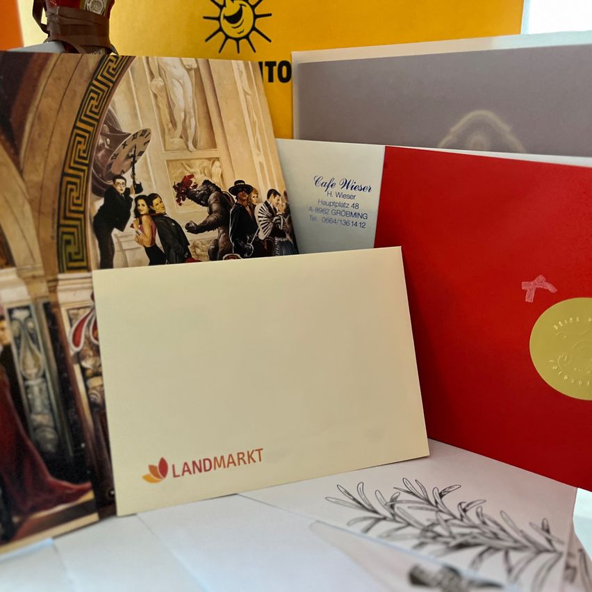 Ein Stapel Broschüren und Karten mit einer, auf der das Wort Landmarkt steht. In der Nähe ist ein goldenes Siegel mit einem Logo. Links ist ein farbenfrohes Gemälde.