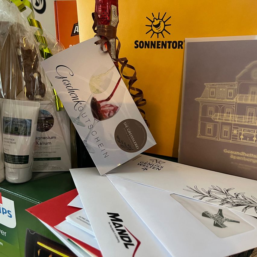 Eine Sammlung von Geschenkartikeln, einschließlich eines Zertifikats, einer Flasche und verschiedener verpackter Produkte, wird auf einer grünen Oberfläche ausgestellt.