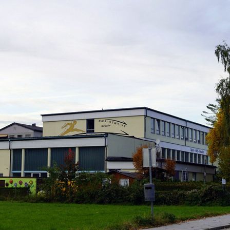 Ein großes Schulgebäude mit einem Läufer-Wandbild ist unter einem bewölkten Himmel zu sehen.