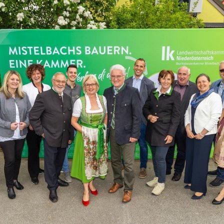 Eine Gruppe von Menschen steht vor einem grünen Schild. Das Schild heißt 'Mistelbachs Bauern. Eine Kammer'. Sie alle lächeln und schauen in die Kamera.