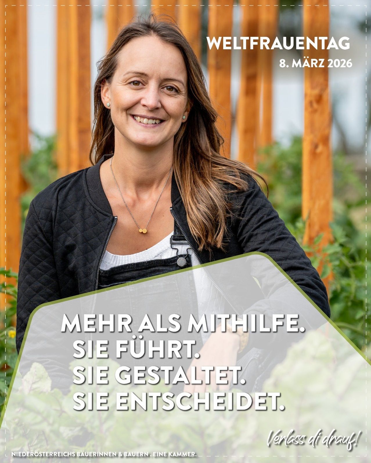 Eine lächelnde Frau in einem Garten mit Holzpfosten, trägt eine schwarze Jacke, Halskette und weißes Hemd. Der Bildtext lautet 'Mehr als Mithilfe. Sie führt. Sie gestaltet. Sie entscheidet.' Datum: 8. März 2026.